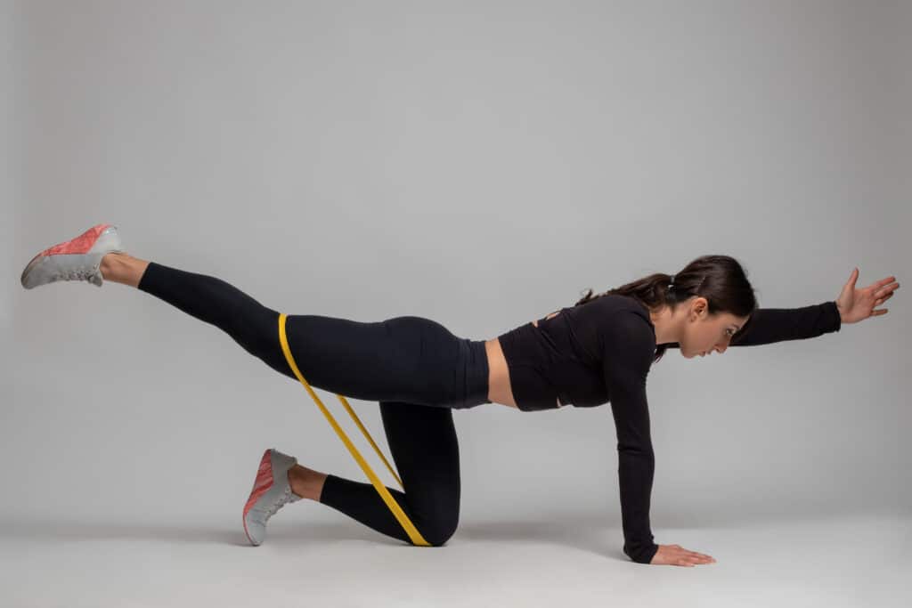 woman doing bird dog stretch with resistance bands