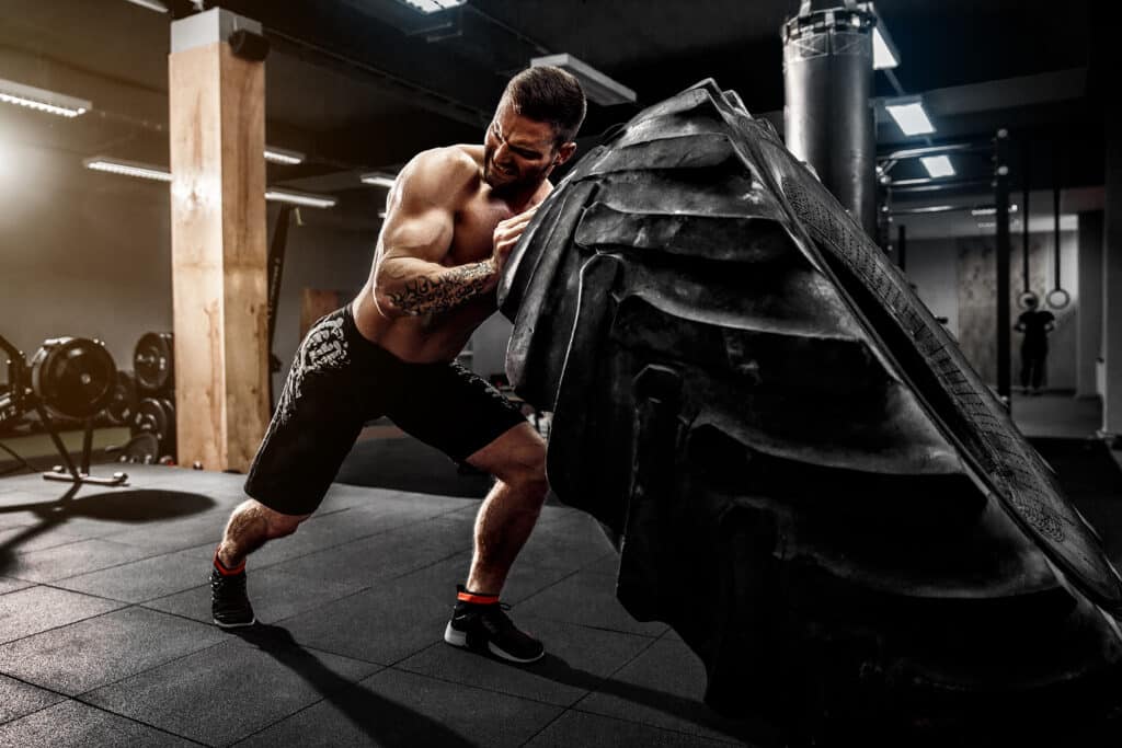 shirtless man flipping heavy tire