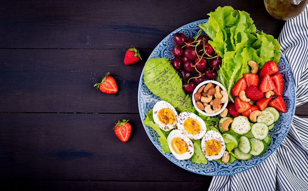 Plate with a paleo diet food. Boiled eggs, avocado, cucumber, nuts, cherry and strawberries. Paleo breakfast. 